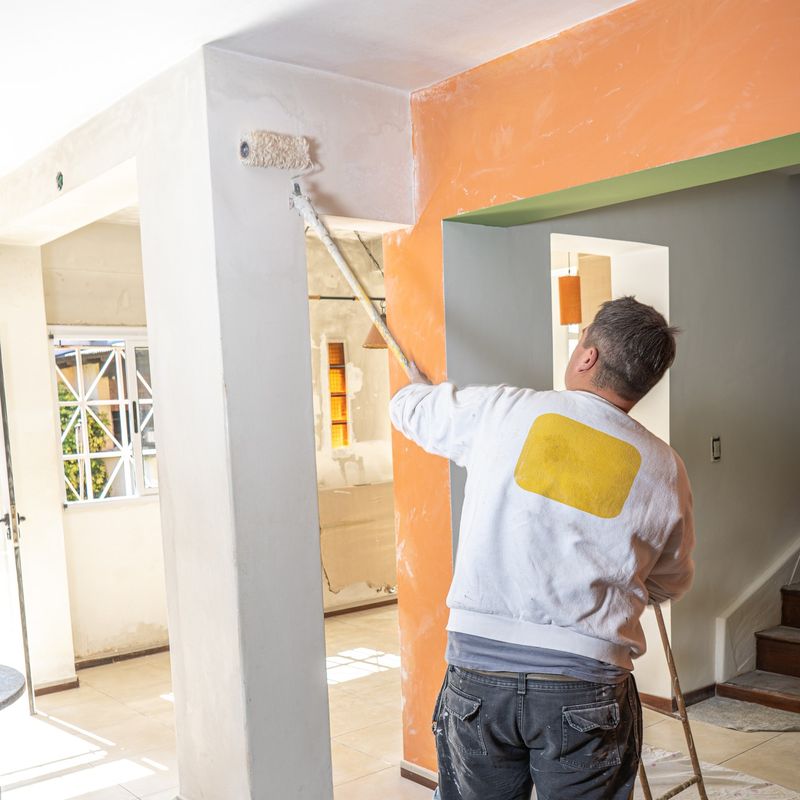 Painter rolling a fresh coat onto an interior wall with the floor protected by drop cloths